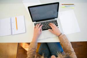 a laptop on a white desk with someone typing on it. 